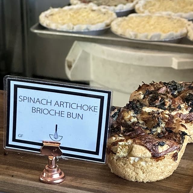 Spinach artichoke brioche buns on a wooden stand beside their case card