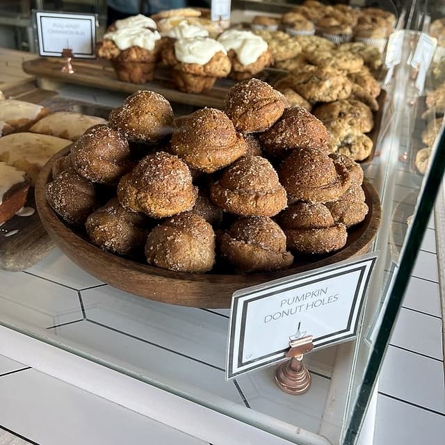 A wooden bowl piled with cinnamon-sugar pumpkin donut holes in the pastry case