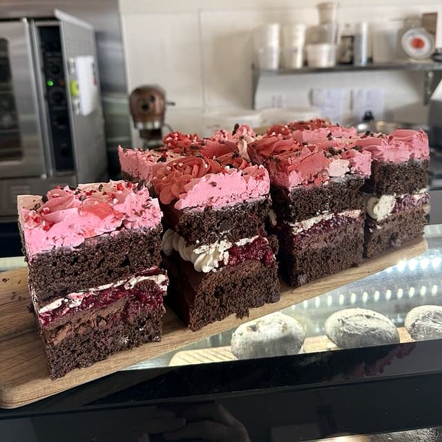 Slices of chocolate layer cake with raspberry filling and pink frosting on a board