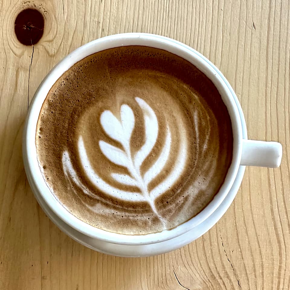 A latte with leaf latte art in a white cup on a wooden table