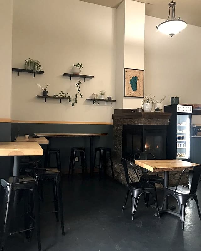 The dining room with wood-topped tables, black chairs, plant shelves and a stone fireplace
